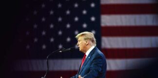 Man in suit speaking in front of American flag.