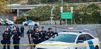Police officers standing by patrol car and barricade tape