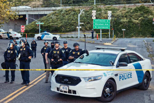 Police officers standing by patrol car and barricade tape