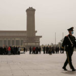 A military guard walking past a crowd at Tiananmen Square in foggy conditions
