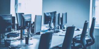 An empty office workspace with multiple computer monitors and chairs