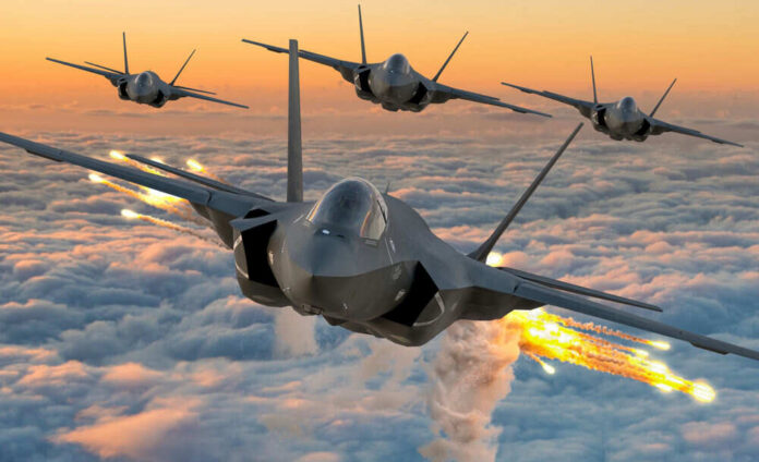 Four fighter jets flying above clouds, firing flares.