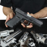 Person holding handgun with revolvers on table