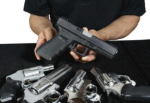 Person holding handgun with revolvers on table