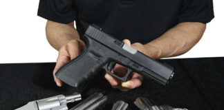 Person holding handgun with revolvers on table