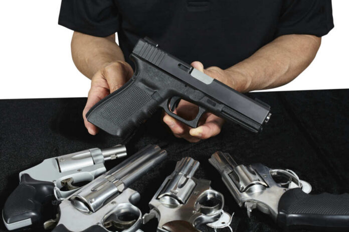 Person holding handgun with revolvers on table