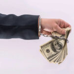 Handcuffed hand holding stack of hundred dollar bills