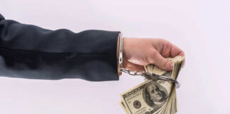 Handcuffed hand holding stack of hundred dollar bills