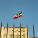 Iranian flag waving above a government building against a blue sky