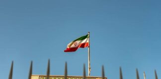 Iranian flag waving above a government building against a blue sky