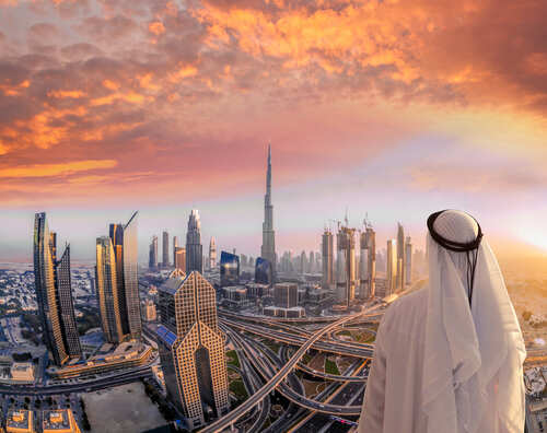 A person in traditional attire overlooking the Dubai skyline at sunset