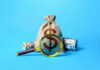 Money bag and magnifying glass on blue background
