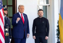 Two men standing outdoors near flags and doorway