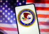 Department of Justice seal on phone, American flag background.