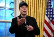 Man wearing hat gesturing in room with flag