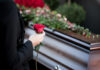 Person holding rose near a wooden coffin