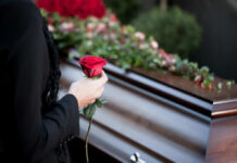 Person holding rose near a wooden coffin