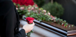 Person holding rose near a wooden coffin