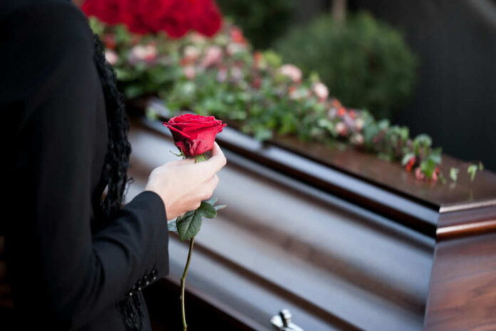 Person holding rose near a wooden coffin