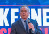 Man speaking in front of large sign with microphone