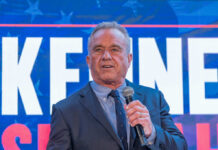 Man speaking in front of large sign with microphone