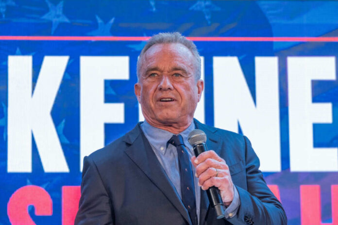 Man speaking in front of large sign with microphone