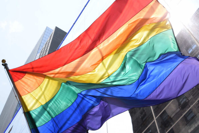 A vibrant rainbow flag waving against a city backdrop