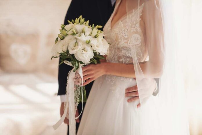 Bride holding a bouquet with groom's hand on her waist