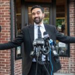 Mamdani’s History Reframe Sparks NYC Debate Man in a suit speaking at a press conference with microphones in front of him