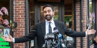 Man in a suit speaking at a press conference with microphones in front of him