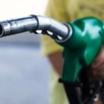 Close-up of a hand holding a green fuel pump nozzle