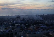 A city skyline at sunset with smoke rising from buildings