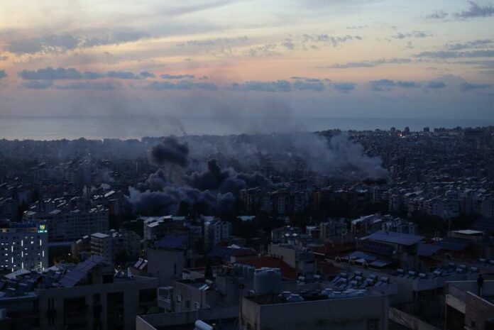 A city skyline at sunset with smoke rising from buildings