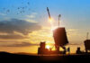 Missile launching at sunset with birds flying nearby.
