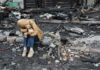 A child sitting on a stone amidst a devastated landscape, holding a teddy bear