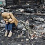 A child sitting on a stone amidst a devastated landscape, holding a teddy bear
