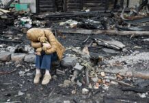 A child sitting on a stone amidst a devastated landscape, holding a teddy bear