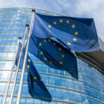 Human Rights Hypocrisy Explodes Across Europe European Union flags waving outside glass building