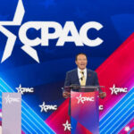 Speaker at CPAC podium on colorful stage backdrop.