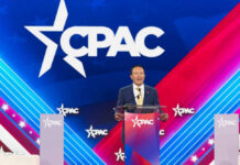Speaker at CPAC podium on colorful stage backdrop.