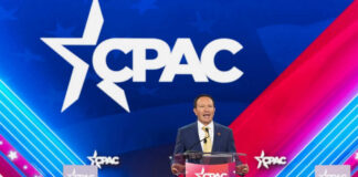 Speaker at CPAC podium on colorful stage backdrop.