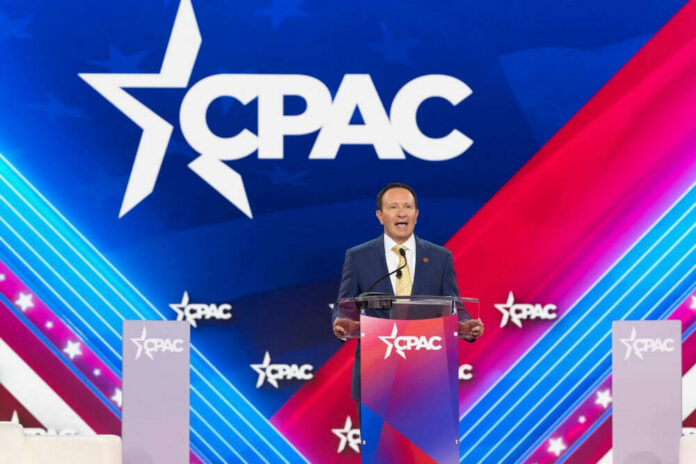 Speaker at CPAC podium on colorful stage backdrop.