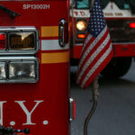 Wind Shifts Fuel Queens Blaze, Injuring 12 Fire trucks with American flag, New York City.