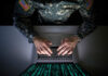 Cheap Phone Data Targets U.S. Bases A soldier in U.S. Army uniform typing on a laptop with green code displayed on the screen
