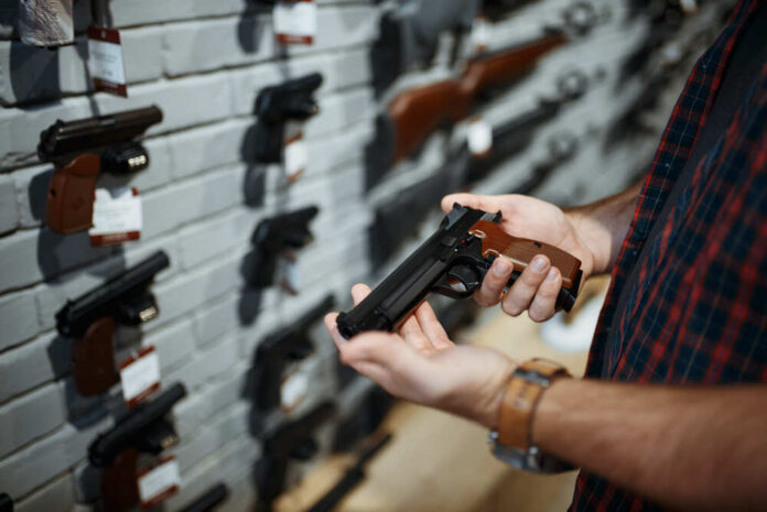 Person holding a handgun in a gun shop with various firearms displayed on the wall