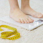 Person standing on a digital scale with a measuring tape nearby