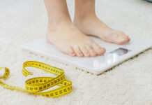 Person standing on a digital scale with a measuring tape nearby