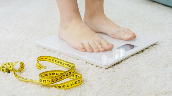 Person standing on a digital scale with a measuring tape nearby