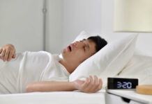A man sleeping in bed with an alarm clock showing 3:20 AM