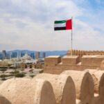 Iranian-Backed Drones Threaten UAE Nuclear Plant! UAE flag waving atop a historic fort with a city skyline in the background